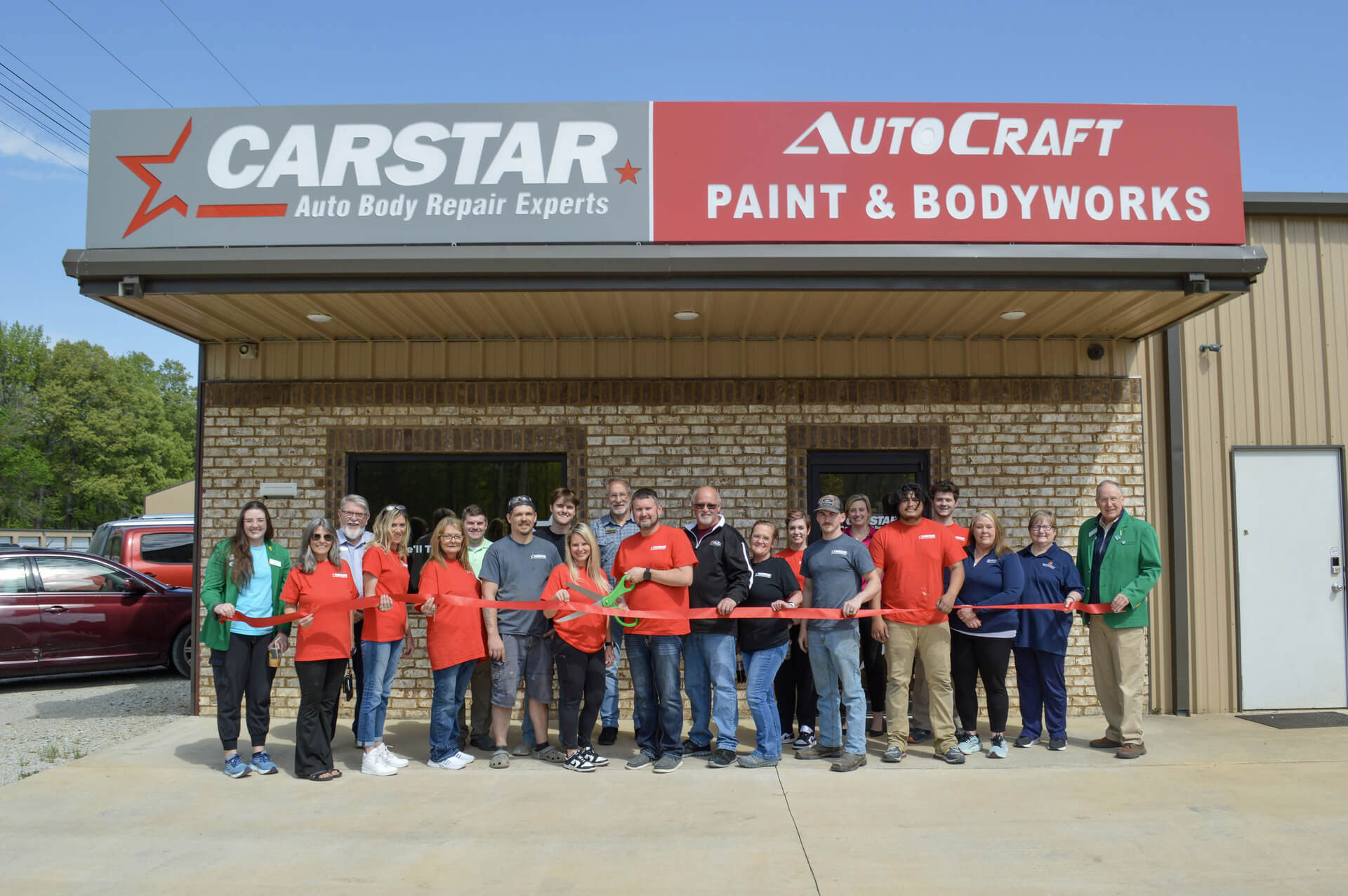 A ribbon cutting for Carstar auto body repair experts outside of their brick building.